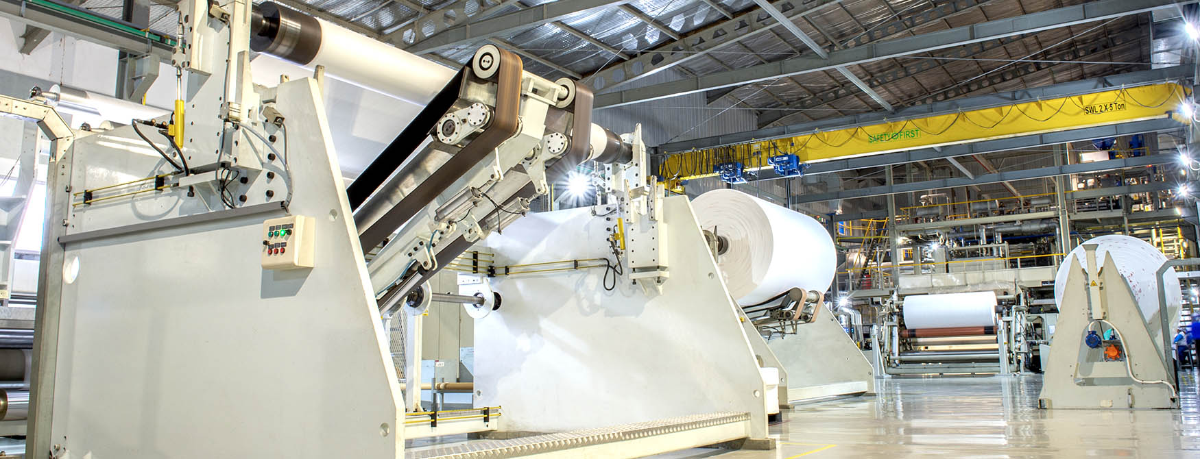 A large bright industrial factory floor showing manufacturing machinery and an overhead crane