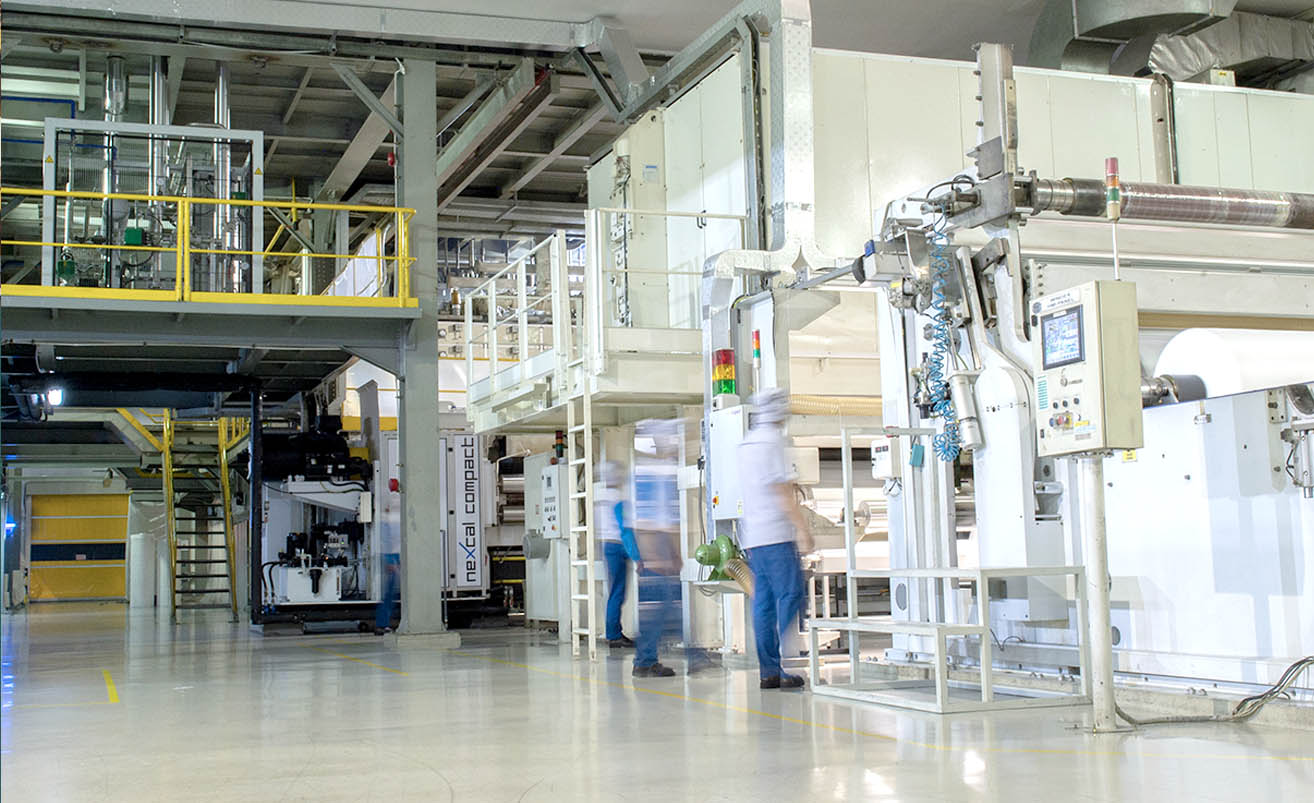 Modern and clean industrial factory setting with large white manufacturing machinery and workers in uniforms