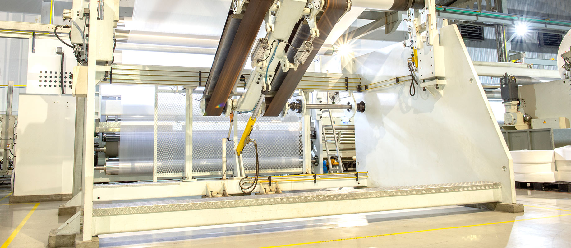 A large industrial manufacturing machine processing white nonwoven fabric on a factory floor