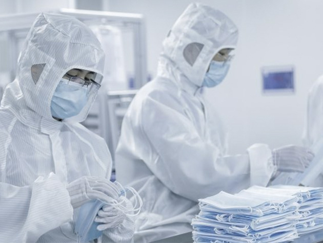 Workers in cleanroom suits manufacturing light blue medical face masks