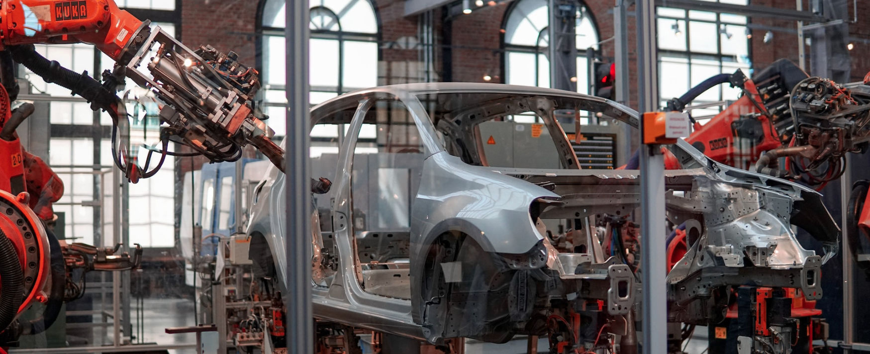 Automated automotive manufacturing assembly line with orange robotic arms working on a car chassis