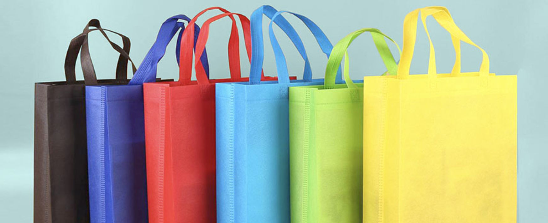 Five colorful reusable nonwoven shopping tote bags lined up