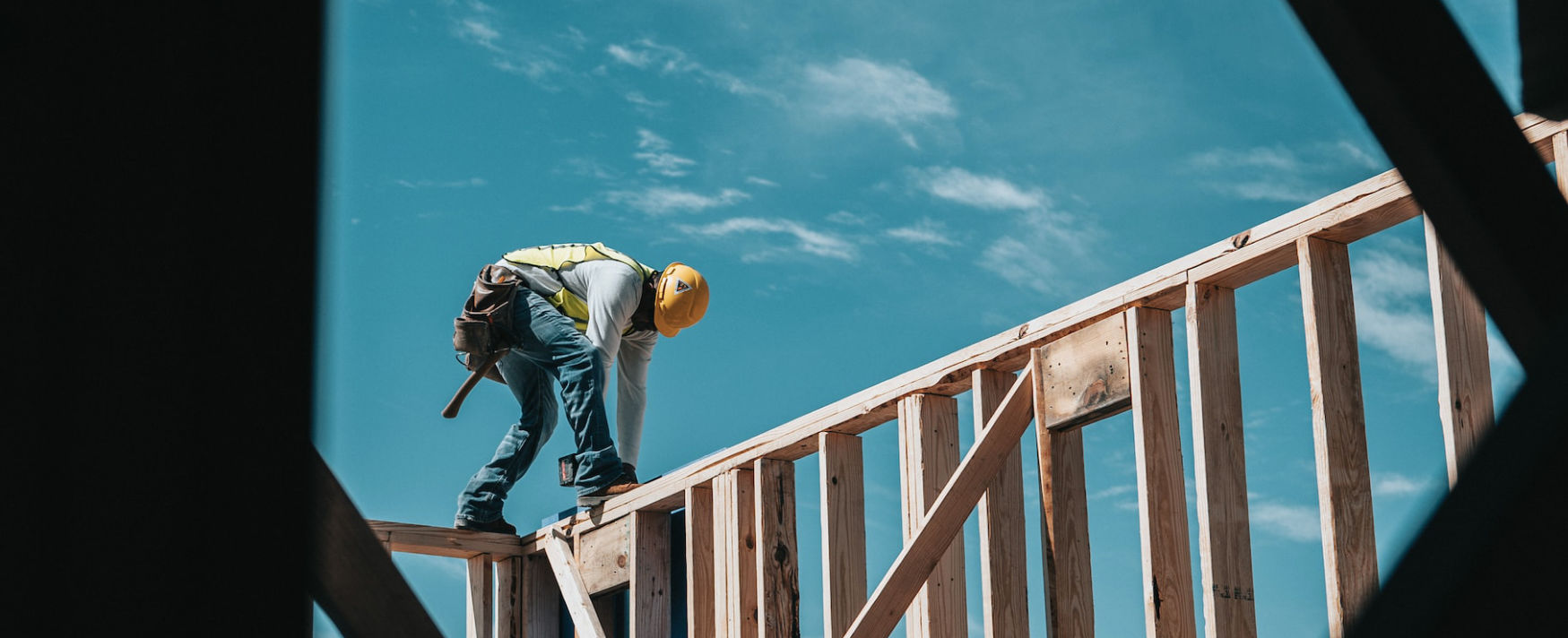 Construction worker in safety gear working on the wooden framing structure of a building