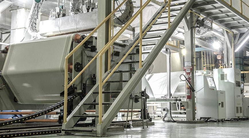 Wide view of a modern factory floor showing stairs, machinery, and white fabric processing