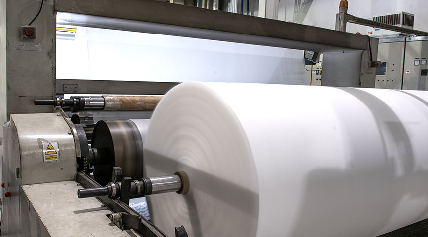 Large roll of white nonwoven material being processed on a machine