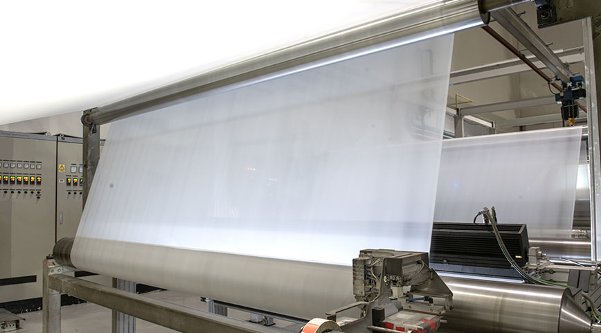 Large sheet of translucent white fabric being rolled on a wide manufacturing machine