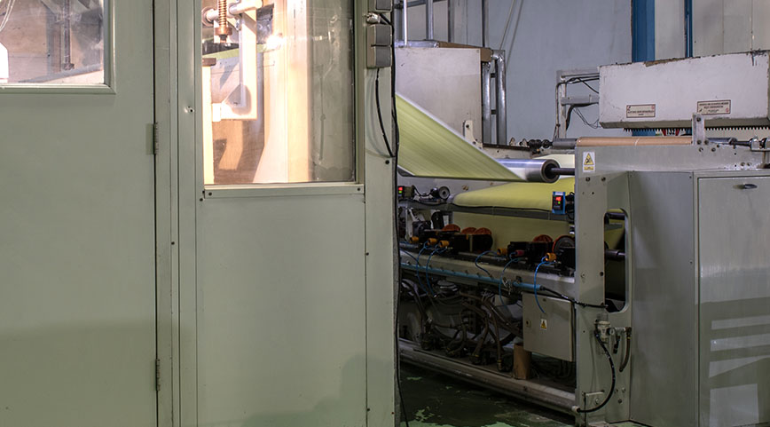 Machine processing pale green or yellow fabric on rollers inside a factory