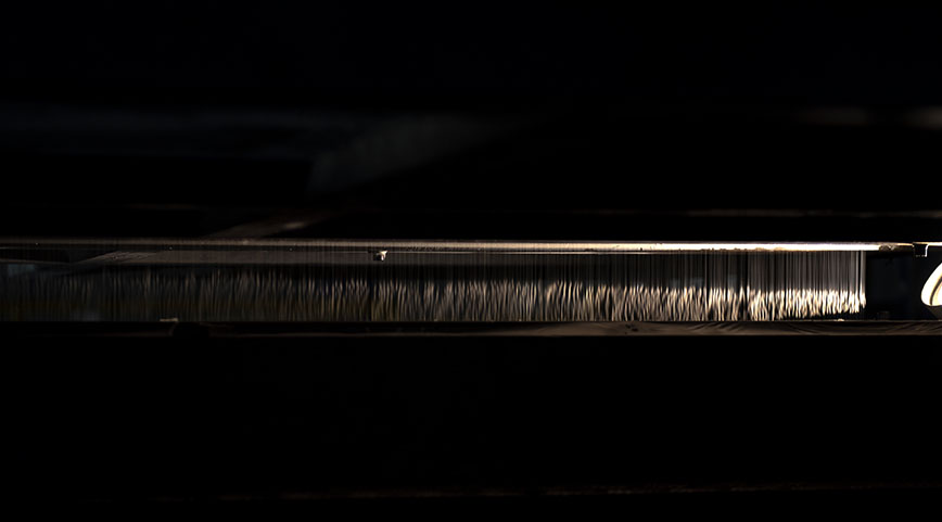 Close-up of a machine with hundreds of fine vertical wires or needles illuminated against a dark background